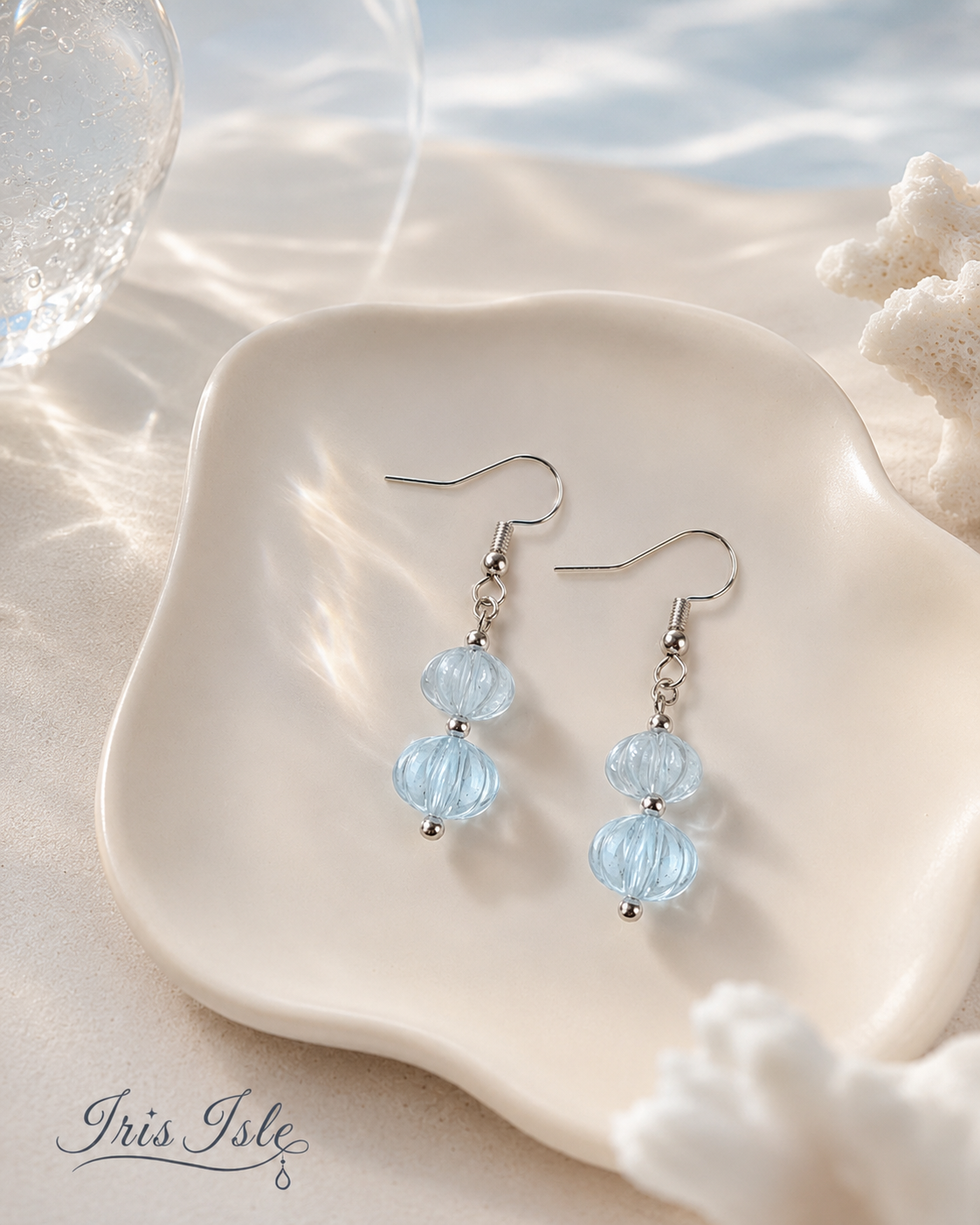 Pale blue lantern-bead drop earrings on a scalloped ceramic dish with coral