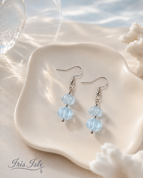 Pale blue lantern-bead drop earrings on a scalloped ceramic dish with coral