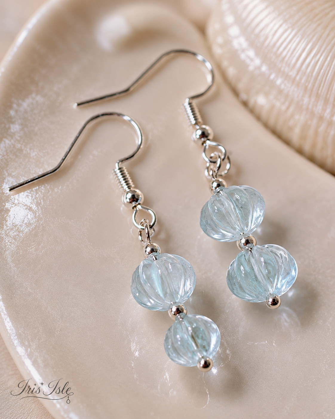 Close-up of translucent blue ribbed bead earrings on a cream ceramic dish
